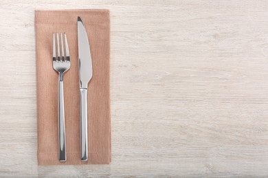 Photo of Shiny fork, knife and napkin on white wooden table, flat lay. Space for text