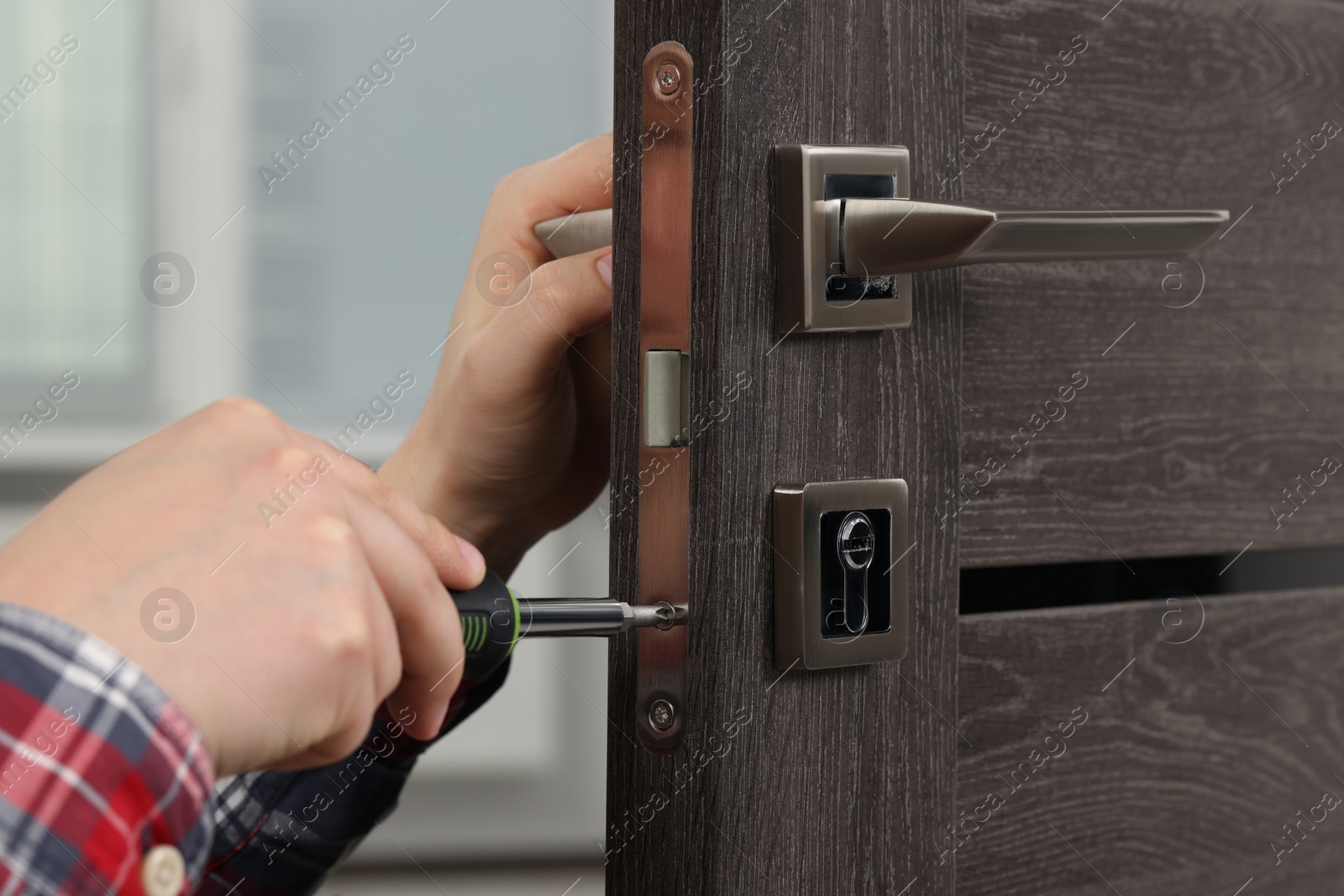 Photo of Handyman with screwdriver repairing door lock indoors, closeup