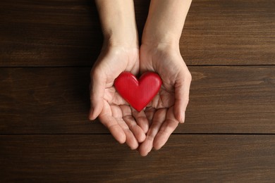 Photo of Elderly woman holding red heart in hands at wooden table, top view