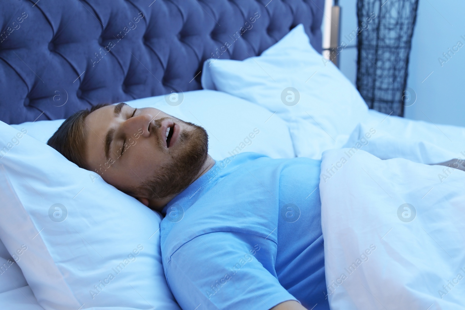 Photo of Young man snoring while sleeping in bed at night. Sleep disorder