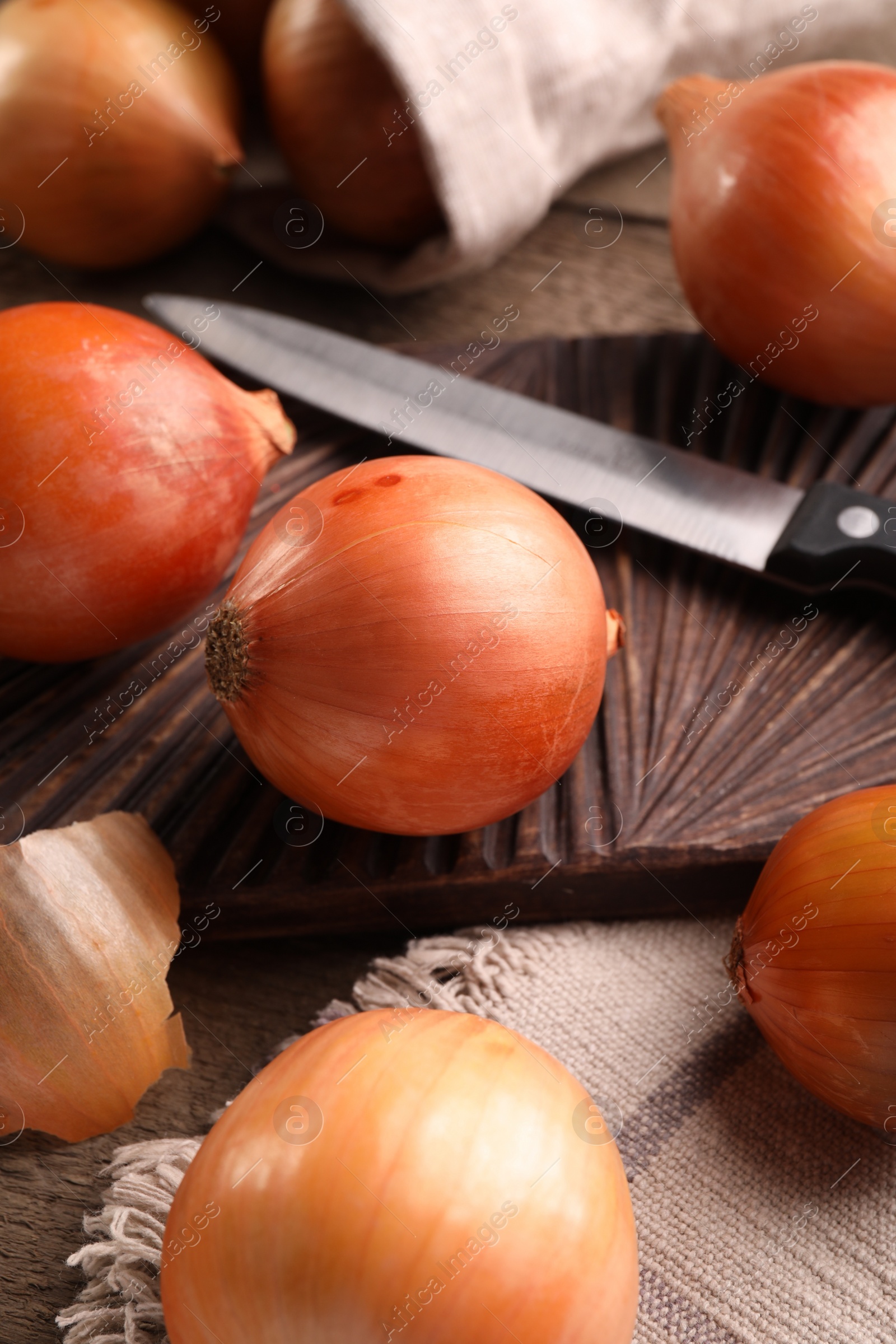 Photo of Many ripe onions and knife on wooden table, closeup