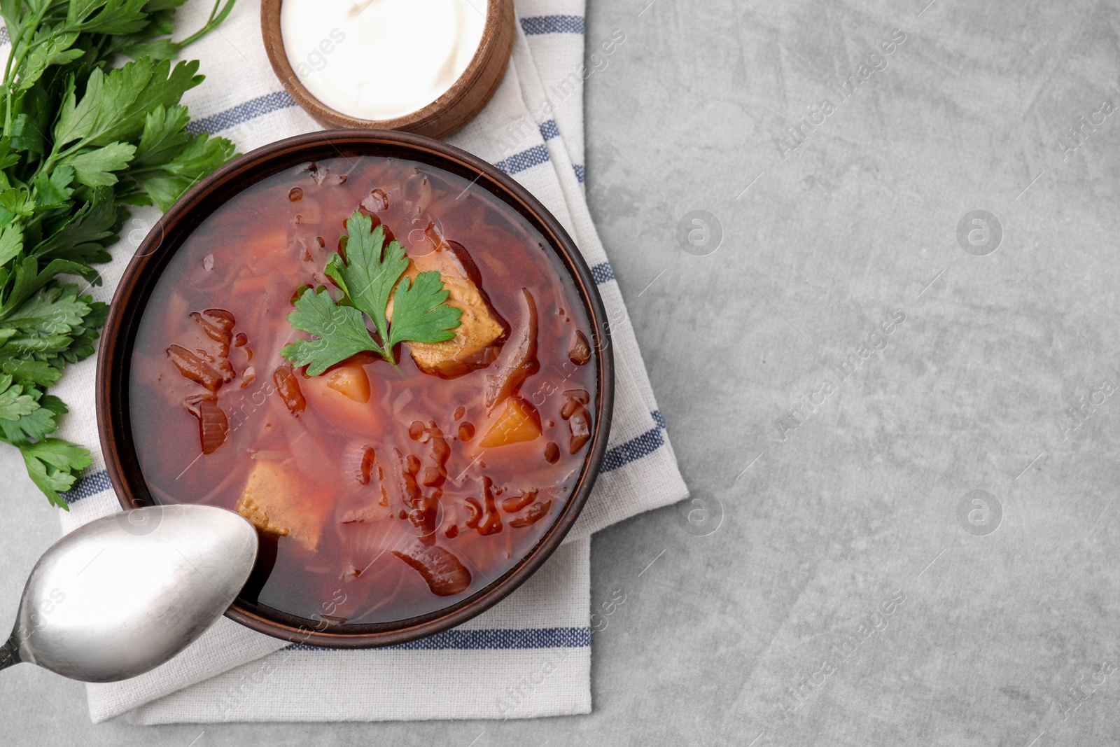 Photo of Bowl of delicious borscht, parsley and sour cream on light grey table, top view. Space for text