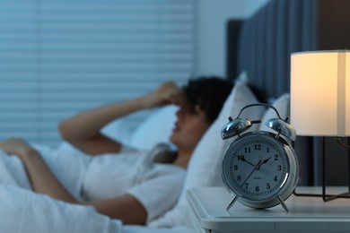 Photo of Young woman suffering from headache in bed at night, focus on alarm clock