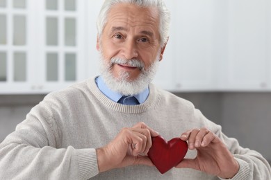 Senior man with red decorative heart indoors