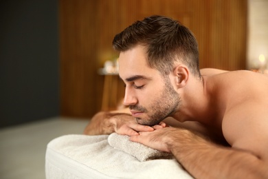 Photo of Handsome man relaxing on massage table in spa salon