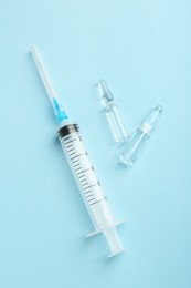 Photo of Glass ampoules with liquid and syringe on light blue background, flat lay