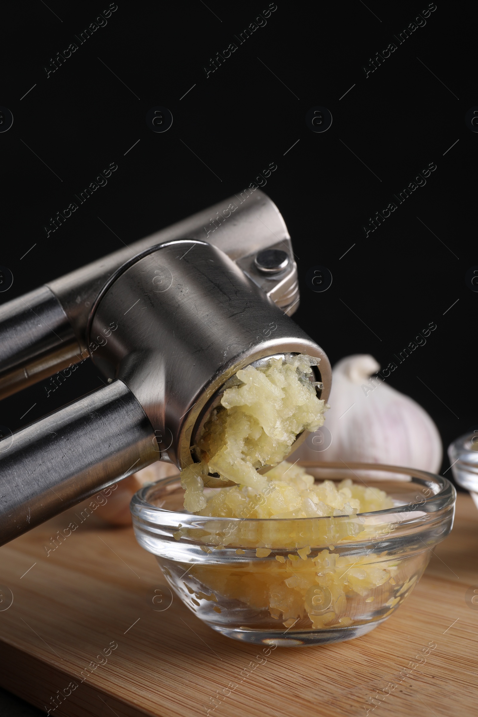 Photo of Crushing garlic with press into bowl at wooden table, closeup