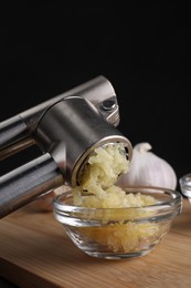 Crushing garlic with press into bowl at wooden table, closeup