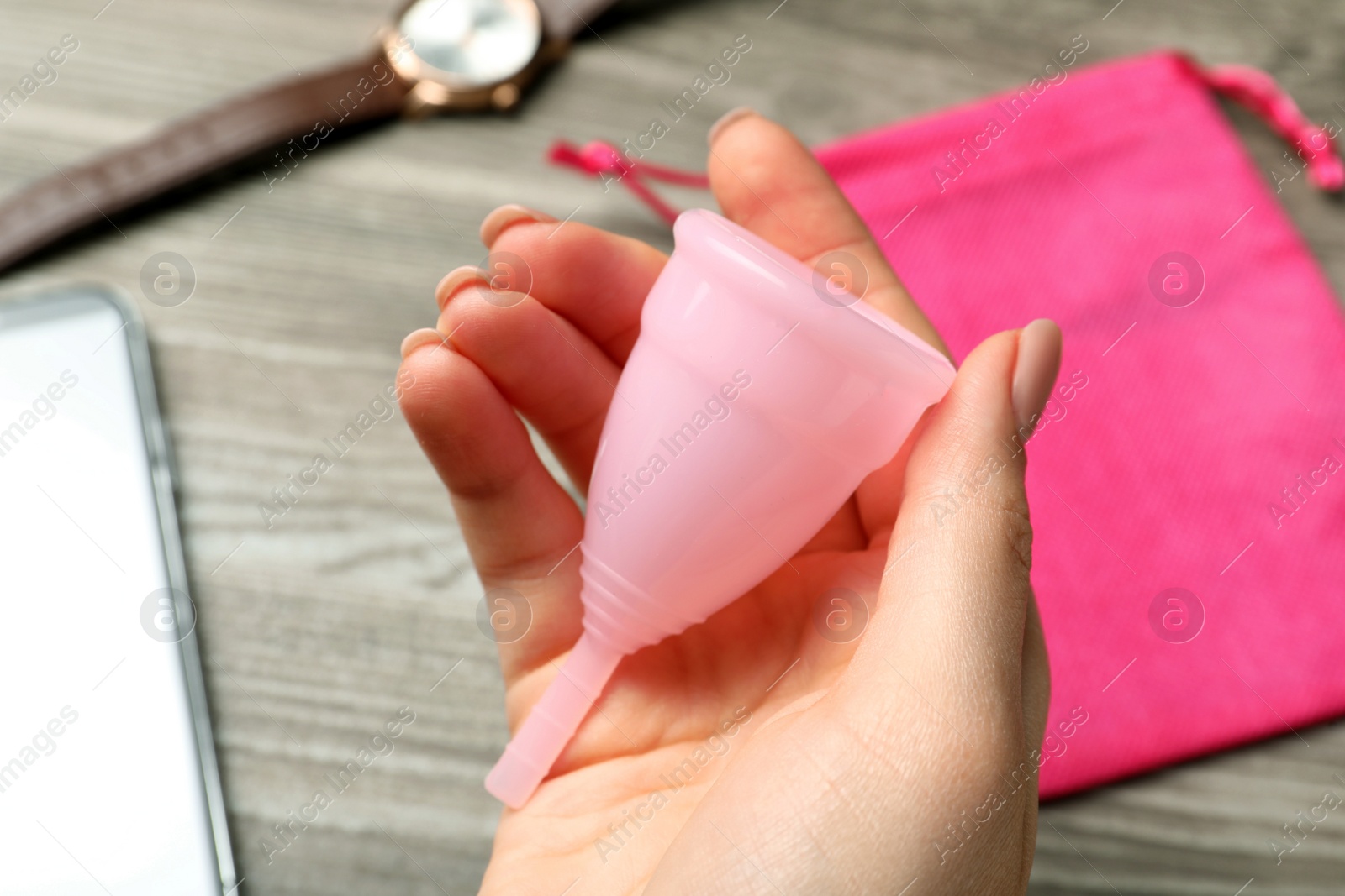 Photo of Woman holding pink menstrual cup over table, closeup