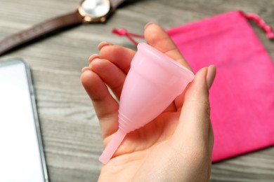 Woman holding pink menstrual cup over table, closeup