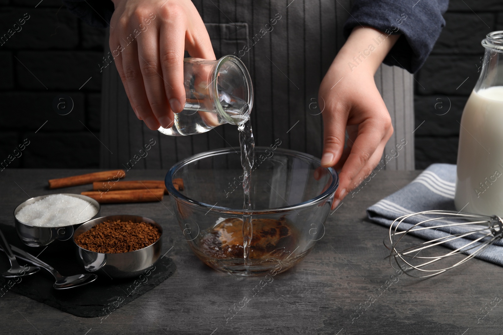 Photo of Making dalgona coffee. Woman pouring water into bowl at grey table, closeup