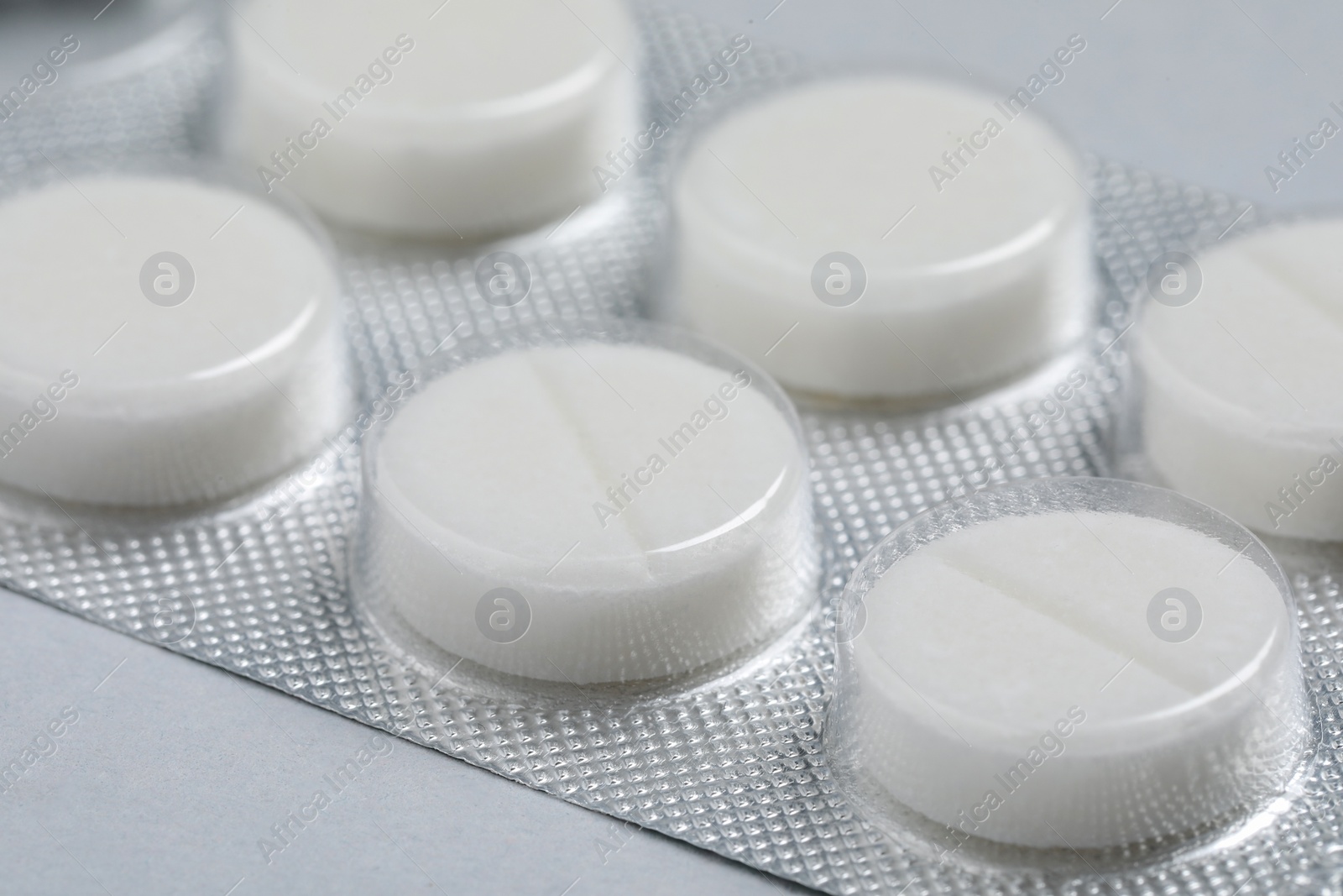 Photo of White pills in blister on grey background, closeup