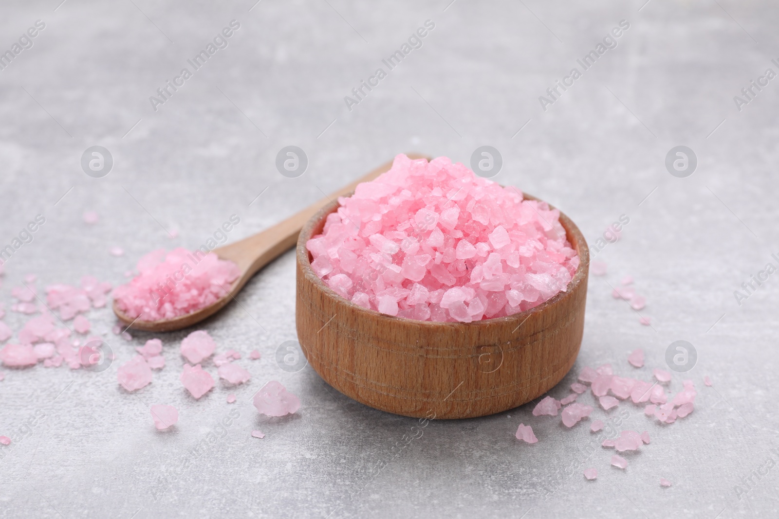 Photo of Bowl and spoon with pink sea salt on light grey table, closeup