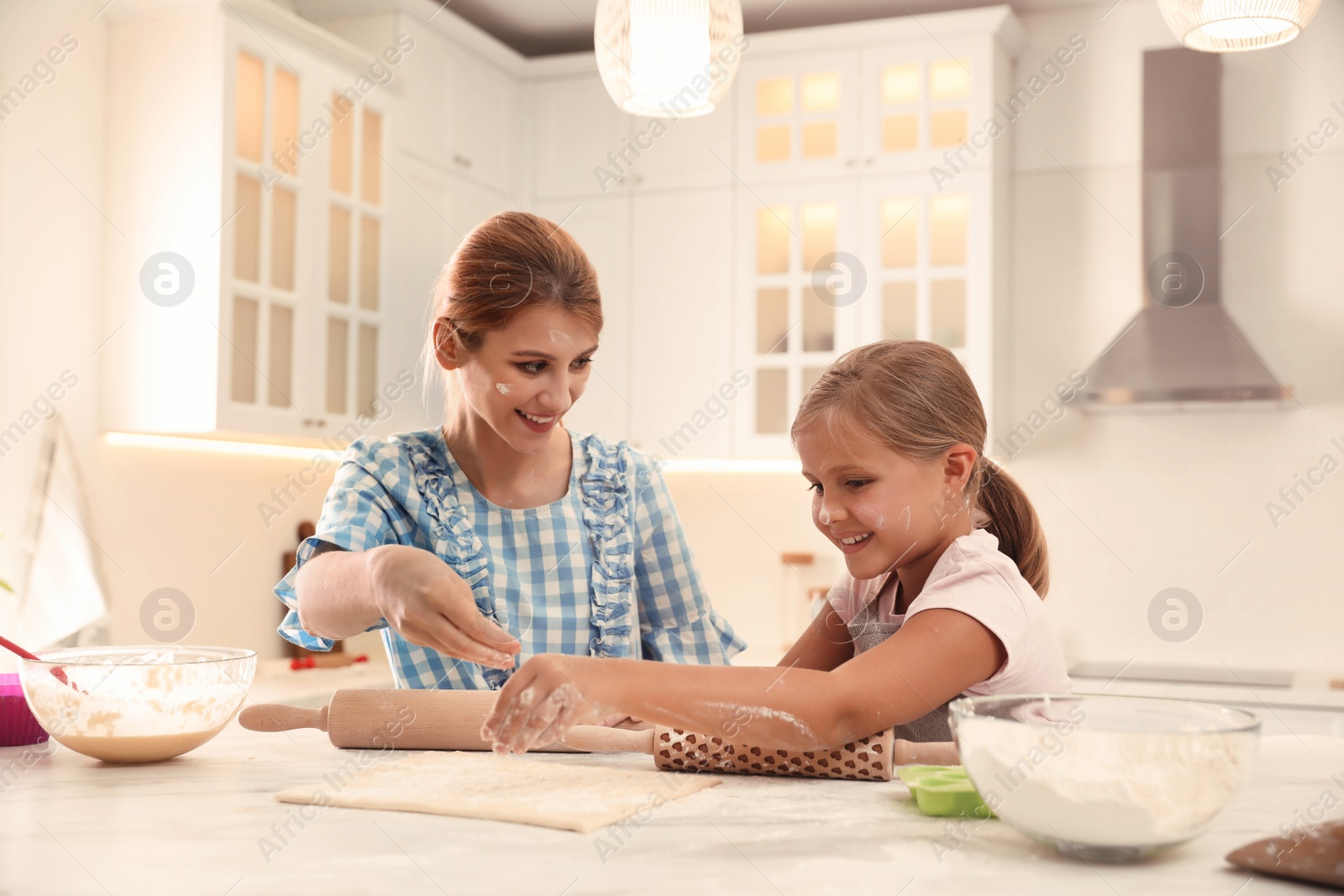 Photo of Mother and daughter rolling dough together in kitchen
