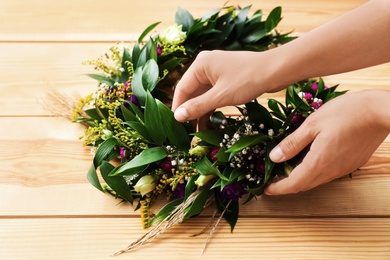 Woman making beautiful wreath of flowers and leaves at wooden table, closeup