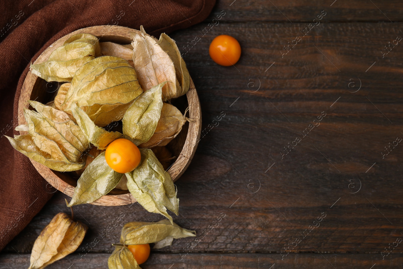 Photo of Ripe physalis fruits with calyxes in bowl on wooden table, flat lay. Space for text