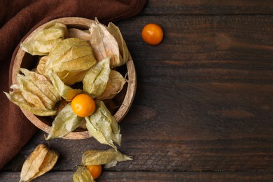 Photo of Ripe physalis fruits with calyxes in bowl on wooden table, flat lay. Space for text