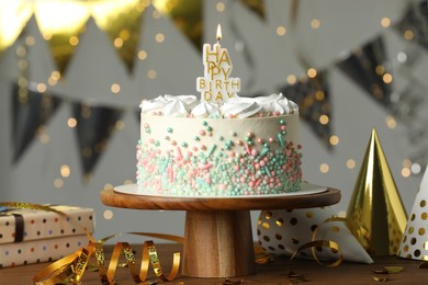 Photo of Beautiful birthday cake with burning candle and decor on wooden table