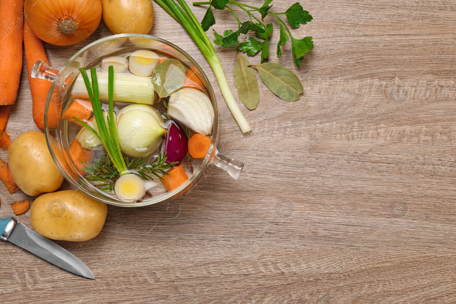 Photo of Glass pot with tasty bouillon and different ingredients on wooden table, flat lay. Space for text