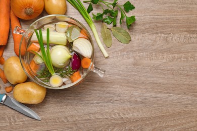 Glass pot with tasty bouillon and different ingredients on wooden table, flat lay. Space for text