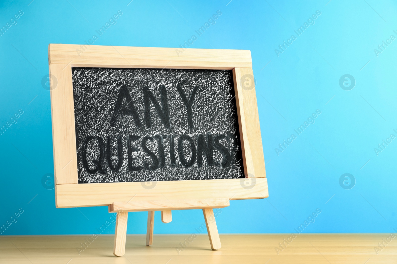 Photo of Blackboard with phrase ANY QUESTIONS on wooden table against blue background