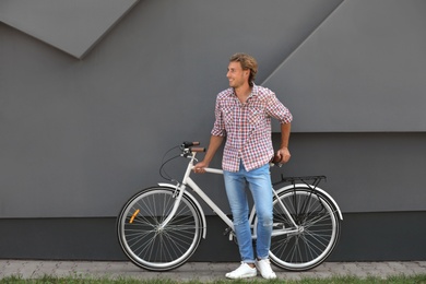 Handsome young man with bicycle near gray wall outdoors