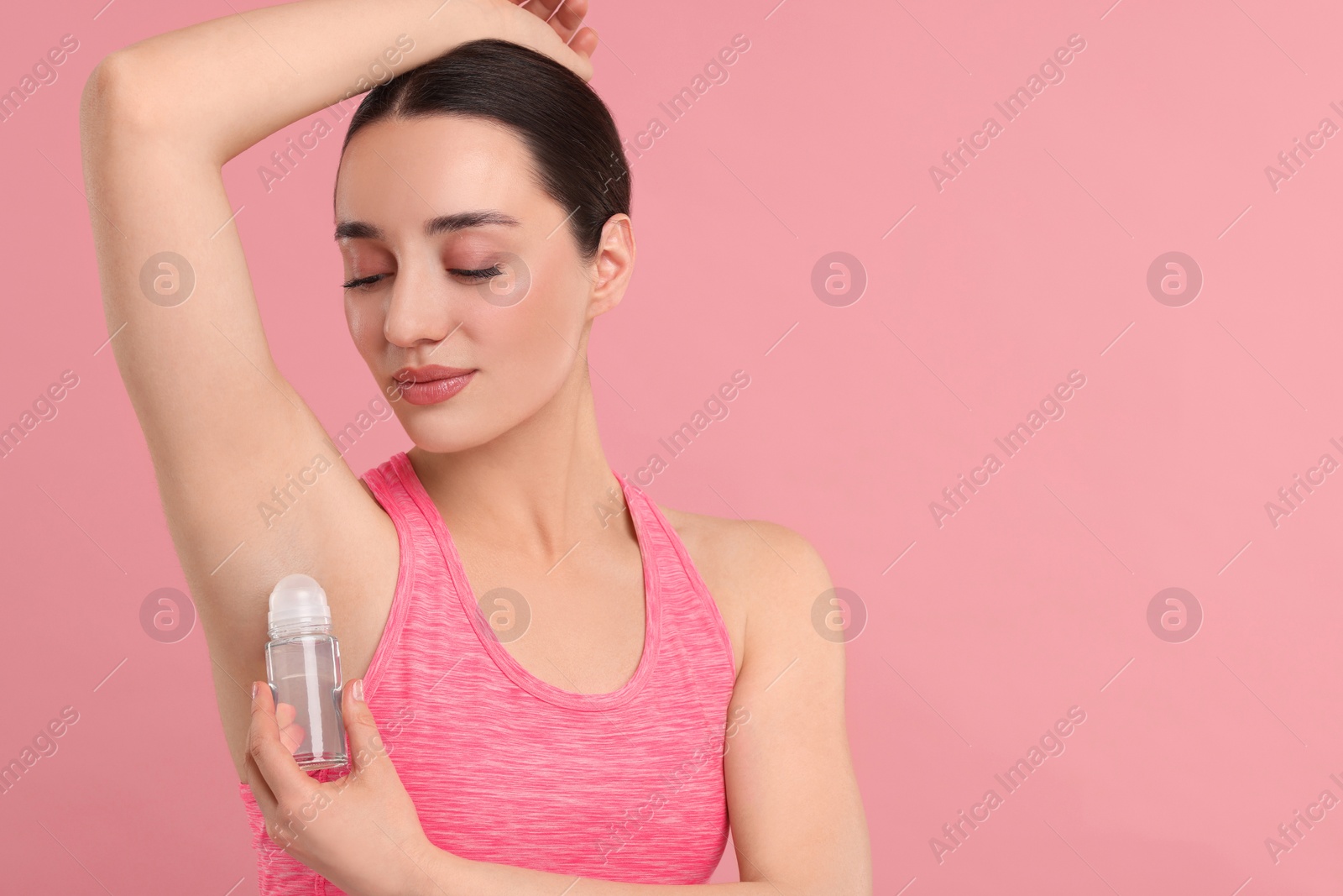 Photo of Beautiful woman applying deodorant on pink background, space for text