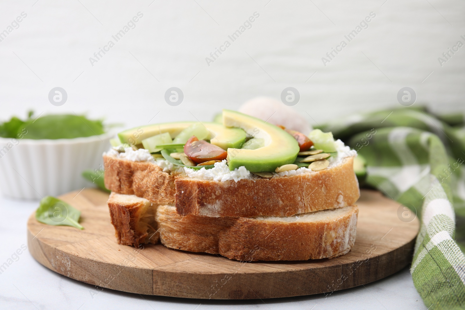 Photo of Tasty vegan sandwich with avocado, tomato and spinach on white marble table