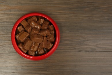 Wet pet food in feeding bowl on wooden background, top view. Space for text