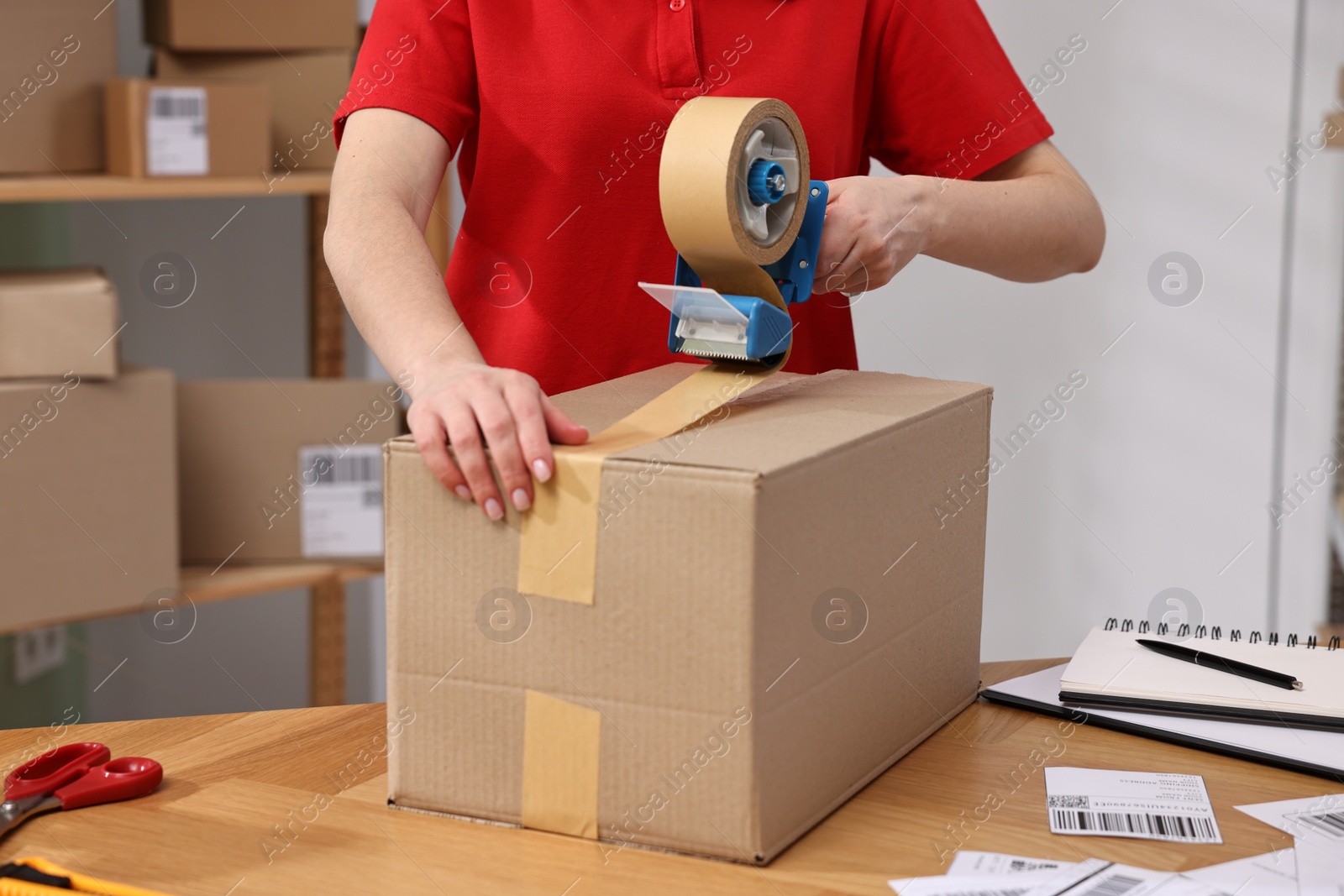 Photo of Parcel packing. Post office worker taping box at wooden table indoors, closeup