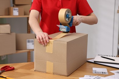 Parcel packing. Post office worker taping box at wooden table indoors, closeup