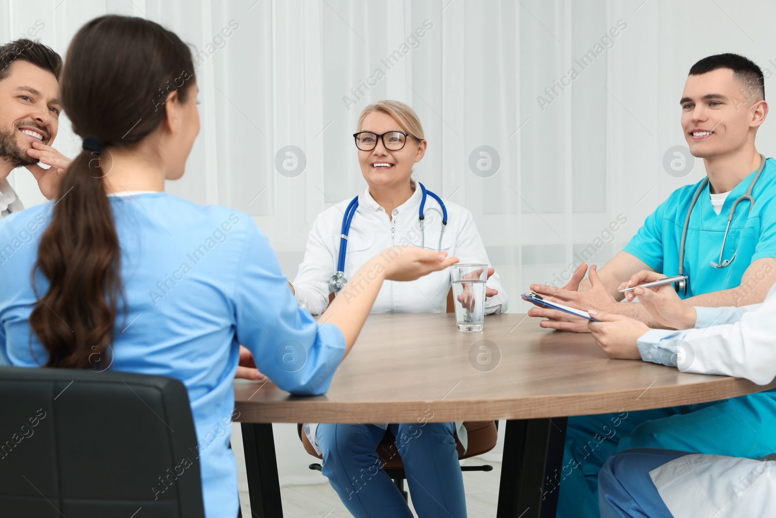 Photo of Medical conference. Team of doctors having discussion at wooden table in clinic