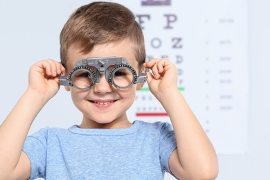 Little boy with trial frame near eye chart in hospital, space for text. Visiting children's doctor