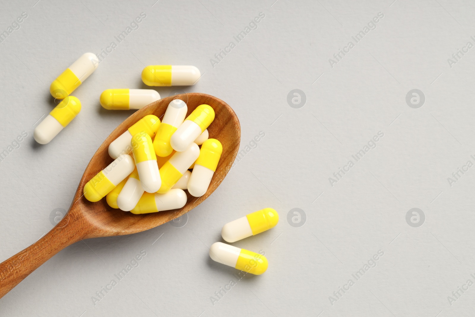 Photo of Many antibiotic pills with wooden spoon and space for text on grey background, top view. Medicinal treatment