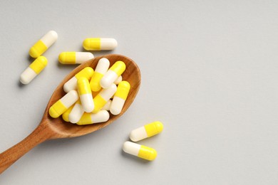 Photo of Many antibiotic pills with wooden spoon and space for text on grey background, top view. Medicinal treatment