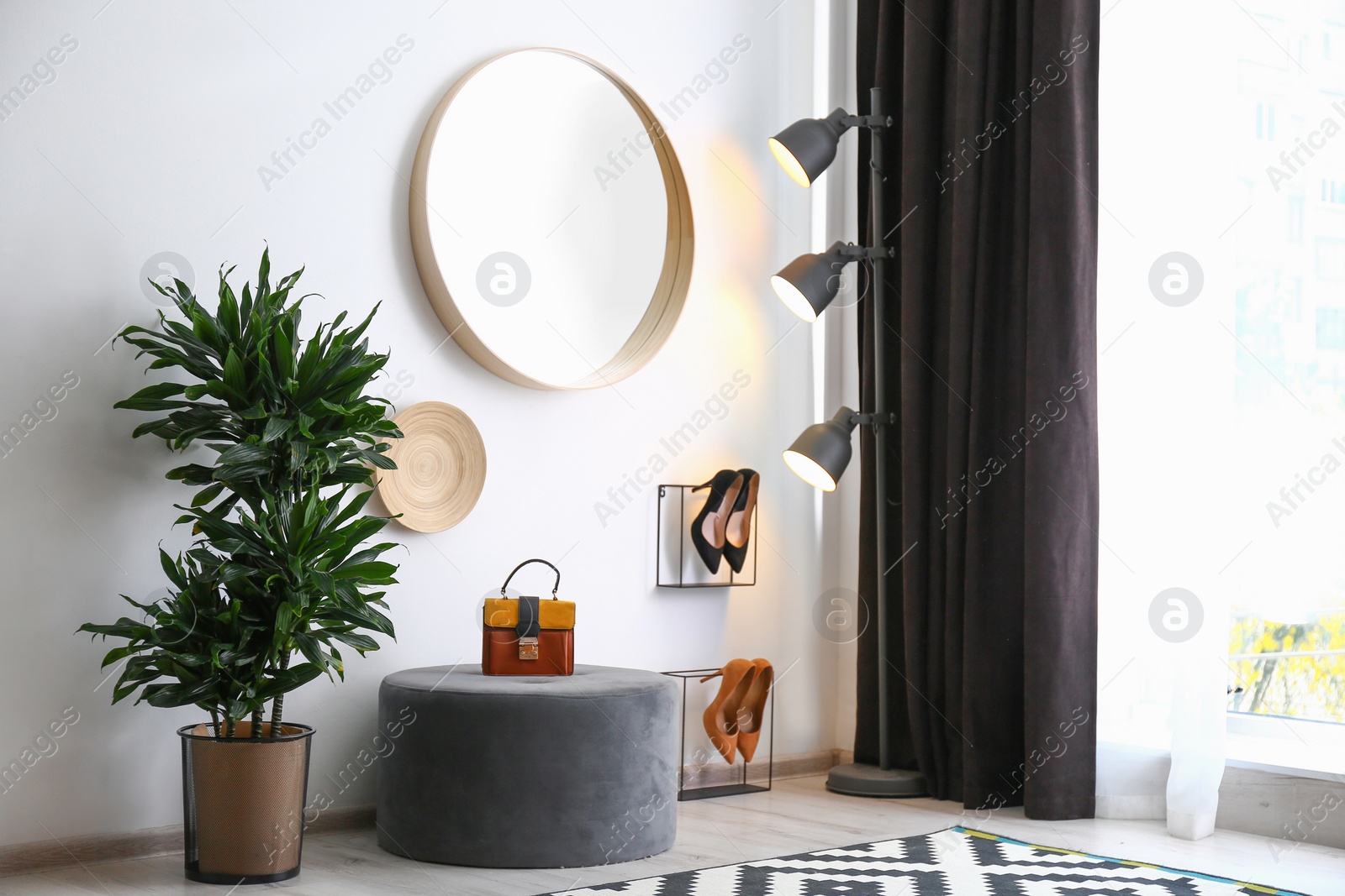 Photo of Hallway interior with big round mirror and ottoman chair near white wall