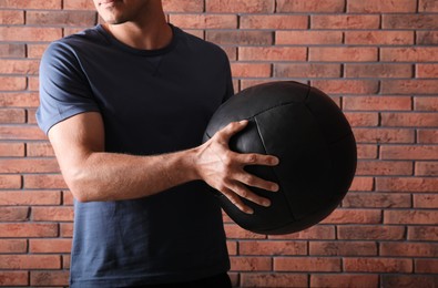 Athletic man with medicine ball near red brick wall, closeup