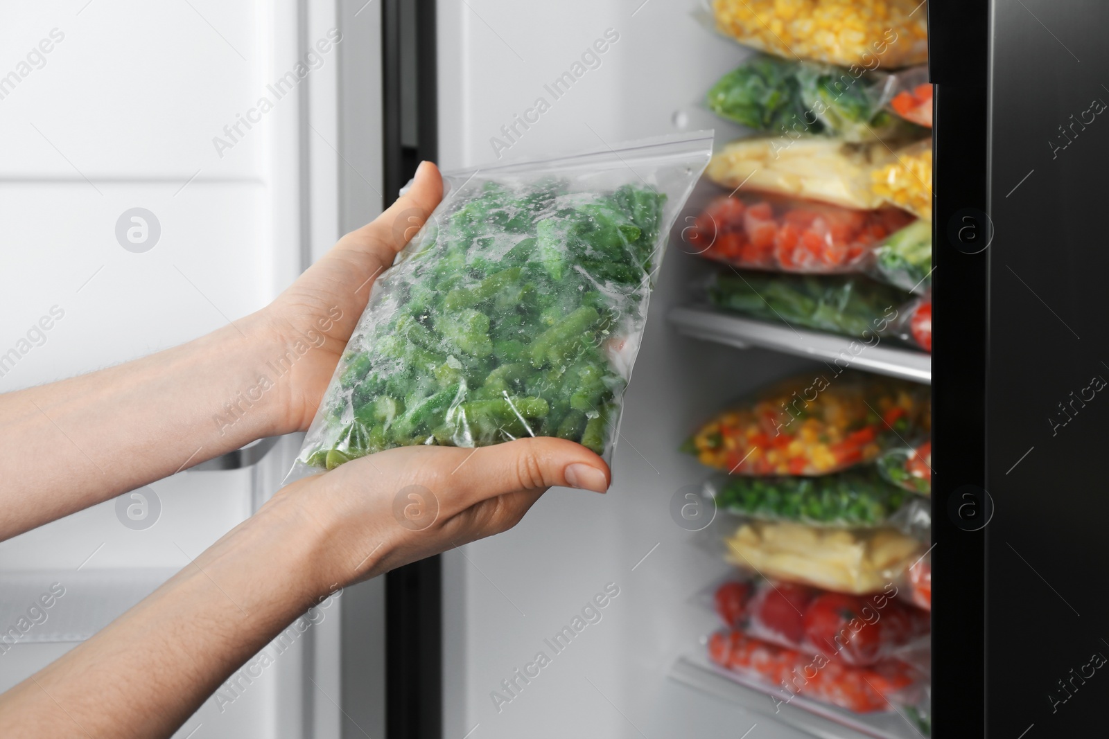 Photo of Woman holding plastic bag with frozen green beans near open refrigerator, closeup