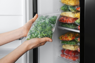 Photo of Woman holding plastic bag with frozen green beans near open refrigerator, closeup