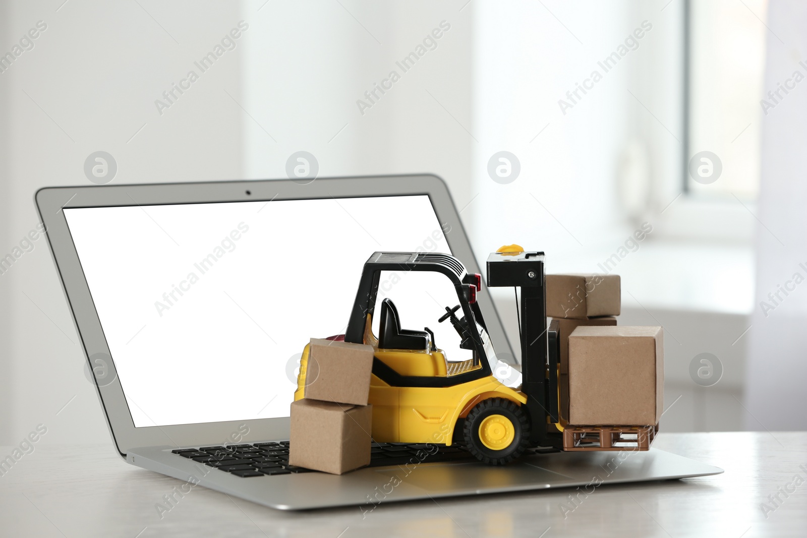 Photo of Laptop and forklift model with boxes on table indoors. Courier service