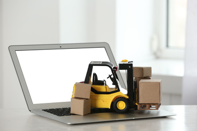 Laptop and forklift model with boxes on table indoors. Courier service