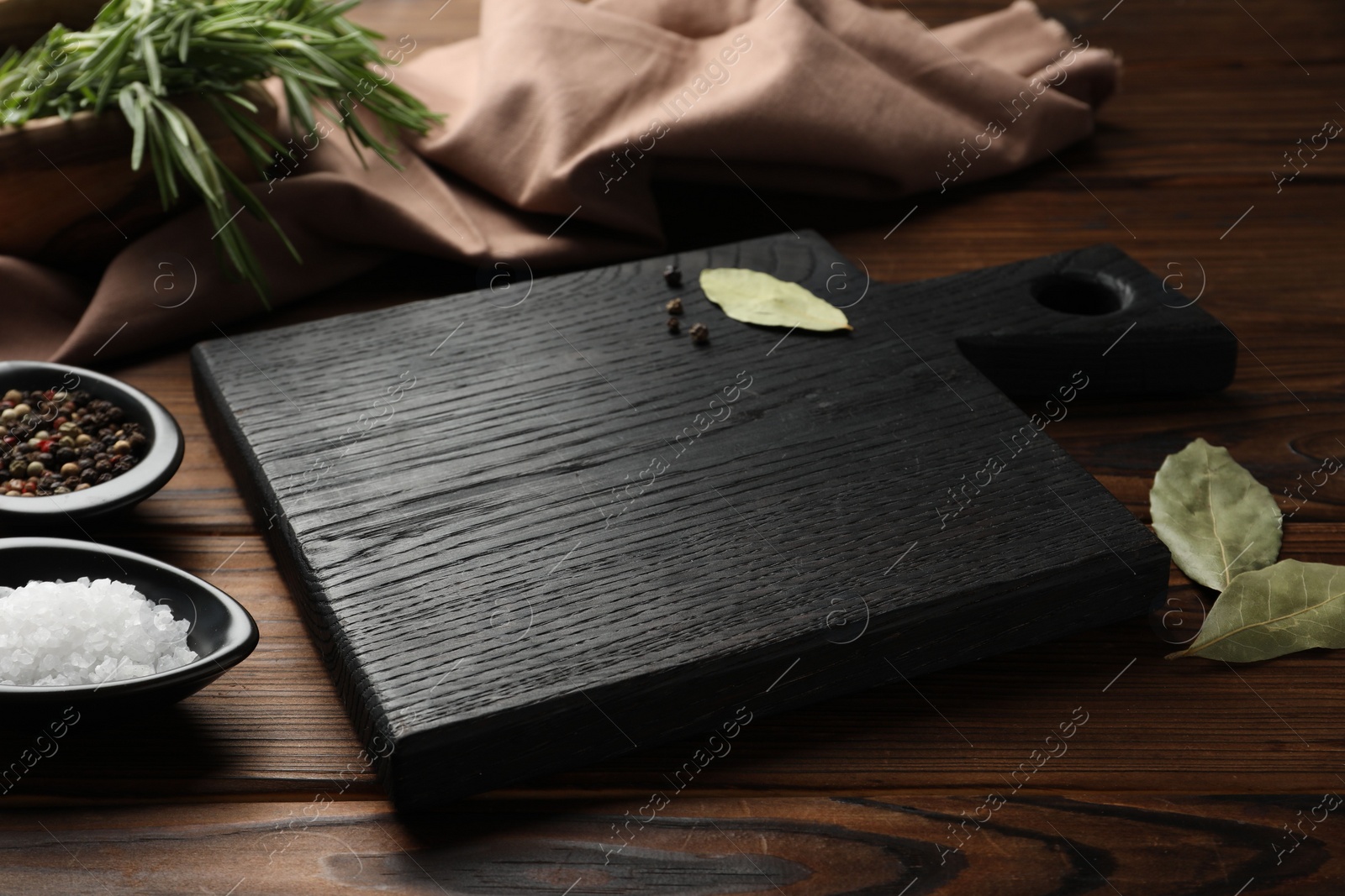 Photo of Black cutting board, salt, pepper and bay leaves on wooden table. Space for text