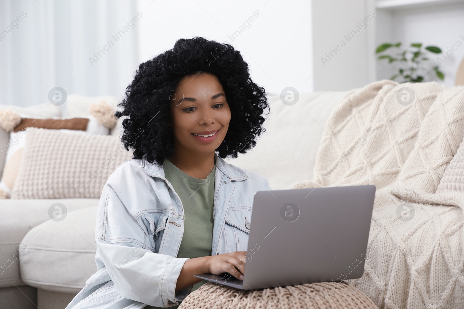 Photo of Happy young woman using laptop on pouf at home