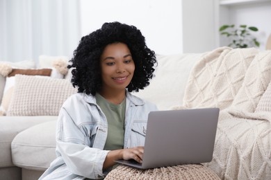 Happy young woman using laptop on pouf at home