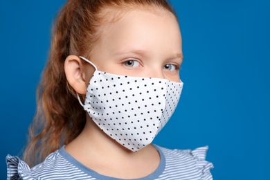 Photo of Preteen girl in protective face mask on blue background, closeup