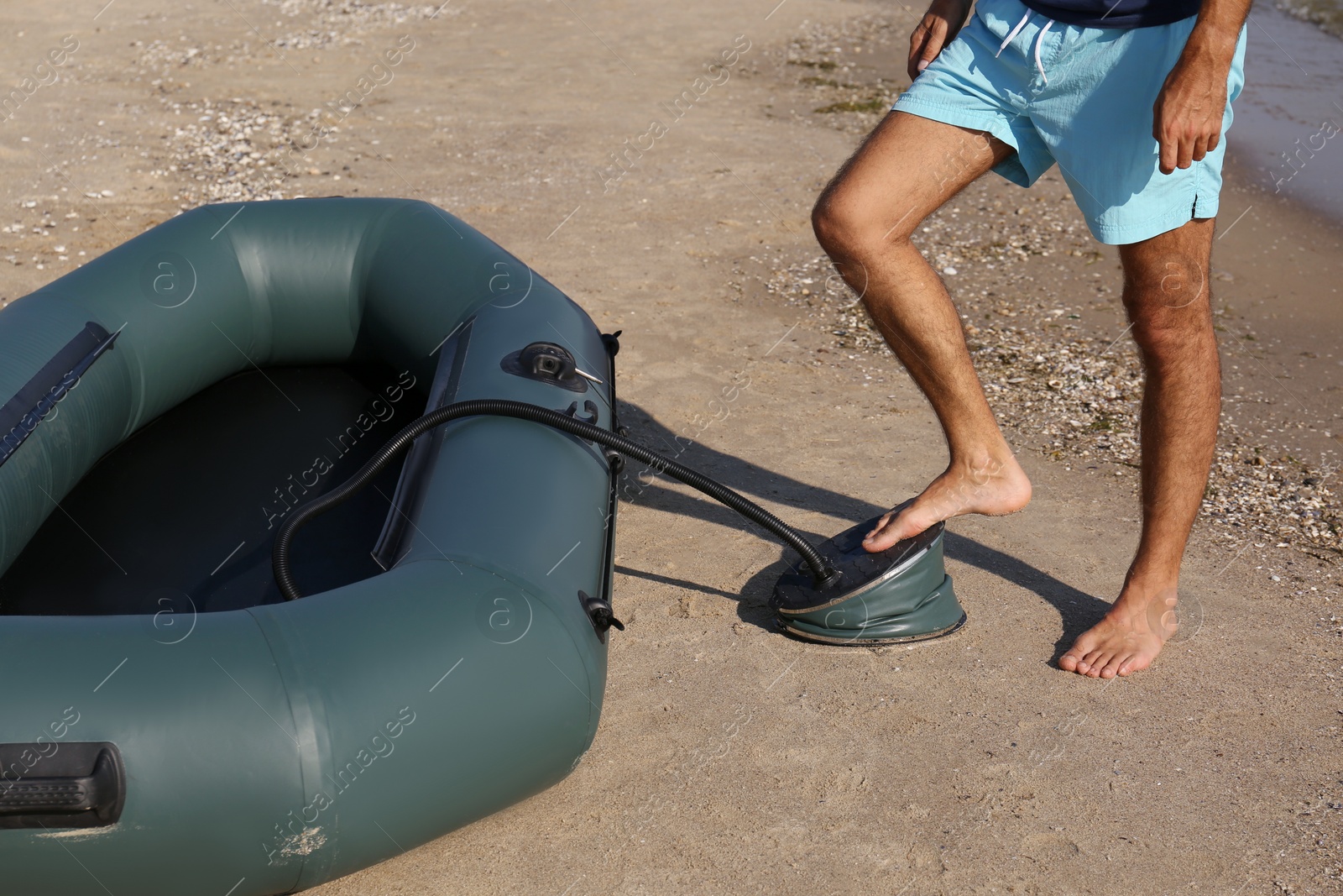 Photo of Man pumping inflatable rubber fishing boat at sandy beach on sunny day, closeup