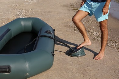 Man pumping inflatable rubber fishing boat at sandy beach on sunny day, closeup