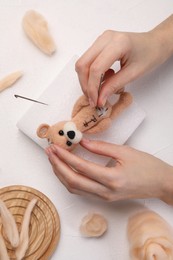 Photo of Woman felting toy bear from wool at white table, top view
