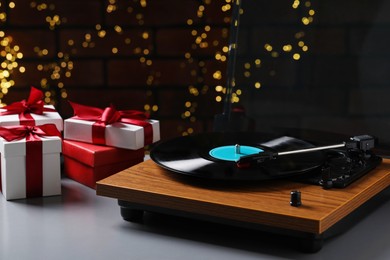 Photo of Turntable with vinyl record and Christmas gift boxes against blurred lights, space for text