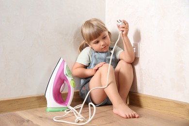 Little child playing with iron plug near electrical socket at home. Dangerous situation